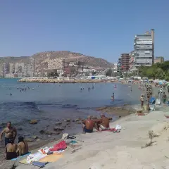 Gente disfrutando del sol y el mar en la playa de la Almadraba, con edificios modernos al fondo.