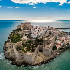 Castillo de Peñíscola sobre el mar, con sus murallas y casas blancas. La peñíscola playa se extiende a su lado, invitando a disfrutar del sol y el Mediterráneo.