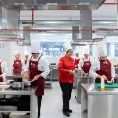 Estudiantes en un centro culinario mediterráneo, con toques rojos y blancos, aprendiendo a cocinar.