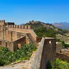 Ruinas del castillo de Sagunto, con sus imponentes murallas de piedra y escalinatas, dominan el paisaje montañoso.