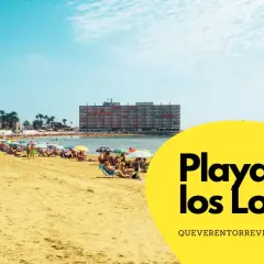 Gente disfrutando del sol y el mar en la **Playa de los Locos**, con sombrillas de colores y edificios al fondo.