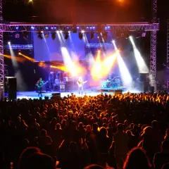 Multitud disfrutando de un concierto en un som festival, con luces brillantes y músicos en el escenario.