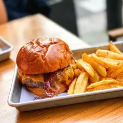 Jugosa hamburguesa con queso fundido y tocino crujiente, acompañada de patatas fritas doradas. Un festín para los sentidos en Hundred Valencia.