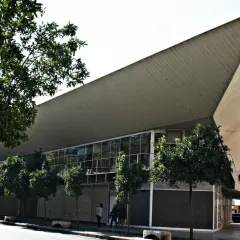 Edificio moderno con techo triangular y árboles en la calle frente al mercado de Jesús.