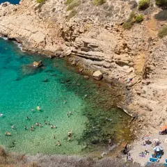 Aguas cristalinas y gente disfrutando en una cala rocosa, un paraíso que recuerda a las mejores calas de Benidorm.