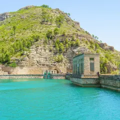 El embalse de Benagéber, con sus aguas turquesas y la imponente presa de piedra, se funde con la montaña verde.