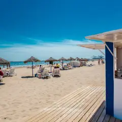 Día soleado en la strand Valencia. Sombrillas, tumbonas y gente disfrutando de la arena dorada y el mar azul.