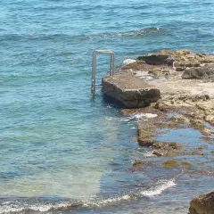 Escalera metálica en una roca que se adentra en el mar azul de cala l'andragó.