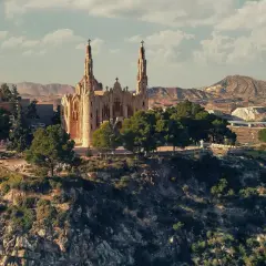 El **santuario** de Novelda se alza majestuoso sobre una colina, rodeado de vegetación y con un paisaje árido de fondo.