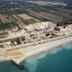 Vista aérea de la costa de Moncofa, con edificios residenciales y campos agrícolas. La playa de Moncofa se extiende hacia el mar turquesa.