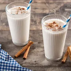 Dos vasos de horchata, bebida refrescante de chufa con canela, sobre mesa de madera.