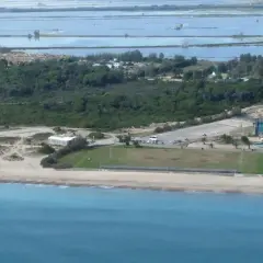 Vista aérea de la costa de El Saler, con el mar azul, la playa, dunas, vegetación, edificios y salinas al fondo.