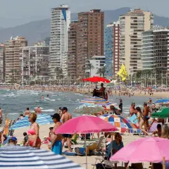 Gente disfrutando de un día soleado en la mejor playa de Benidorm, con edificios altos de fondo y sombrillas de colores.
