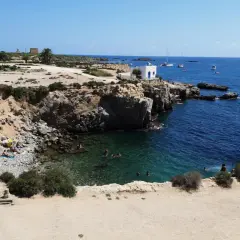 Gente nadando y tomando el sol en las calas de la isla Tabarca, con aguas cristalinas y barcos en el horizonte.