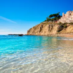 Aguas cristalinas en las calas de Alicante, con una urbanización blanca en la cima del acantilado y el mar azul intenso.