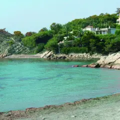 Aguas turquesas bañan la cala d'enmig, con casas blancas y verdes colinas de fondo.