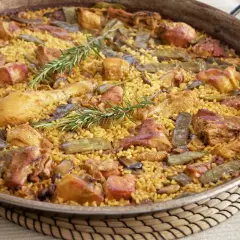 Paella valenciana recién hecha, con arroz amarillo, trozos de pollo, judías verdes y romero fresco.