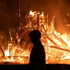 Silueta de persona observando la **cremà** de una falla en **Valencia**. El fuego consume la estructura de madera, creando un espectáculo de llamas y humo.