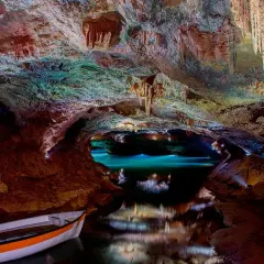 Interior de cueva con estalactitas, agua turquesa y una barca. Consulta las cuevas de Vall d'Uixó horarios y precios para tu visita.