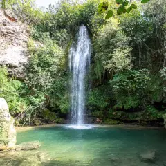 Los chorradores de Navarres, una cascada cae en una poza de agua turquesa rodeada de vegetación exuberante y rocas.