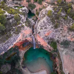Cascada cayendo en una poza turquesa, rodeada de rocas rojizas y vegetación. Un rincón secreto, como la cueva turche, esperando ser descubierto.