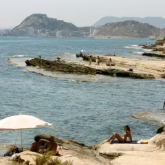 Gente disfrutando del sol y el mar en las playas nudistas de Calpe, con la ciudad al fondo.