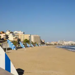 Amplia playa del Moro con edificios turísticos al fondo y sombrillas a rayas azules y blancas alineadas en la arena dorada.