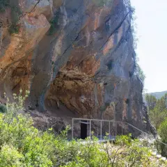 La cueva de la araña, una entrada moderna a una formación rocosa natural, se asoma entre la vegetación.