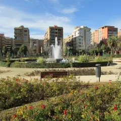 Parque urbano con fuente central y edificios residenciales al fondo. Los viveros de Valencia lucen sus rosales en flor.