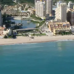 Vista aérea de la playa de la goleta, con edificios residenciales, una laguna artificial y el mar turquesa.