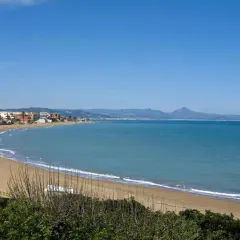 Amplia vista de la playa de Les Bovetes con arena dorada, mar azul y montañas al fondo. Un día soleado perfecto para disfrutar.