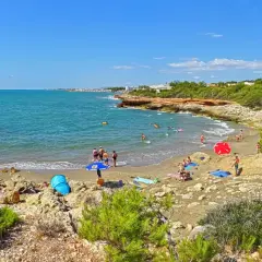 Gente disfrutando del sol y el mar en la cala blanca de Castellón, con aguas turquesas y vegetación mediterránea.