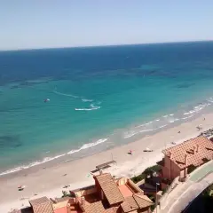 Vista aérea de la Campoamor playa con aguas turquesas, gente disfrutando del sol y un kitesurfista en acción.