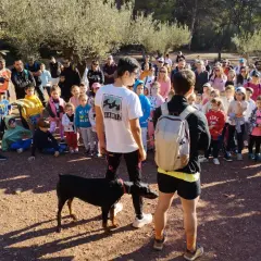 Un grupo de personas, incluyendo niños, se reúne en un sendero boscoso. Un hombre con una camiseta roja toma una foto con su móvil. Un perro Dóberman negro está atado a un joven. Quizás están buscando al **dragón de la Calderona**.