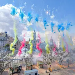 Explosión de color y ruido en la mascletà hoy. El cielo se tiñe de azul, amarillo y rosa sobre edificios históricos.
