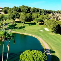 Un hermoso campo de golf con un lago azul, palmeras y un edificio al fondo. El sol ilumina el verde impecable de las ramblas golf.