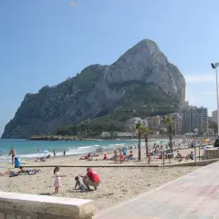 Gente disfrutando del sol y el mar en la playa de la Fossa, con el imponente peñón de Ifach de fondo.