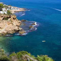 Vista de la cala Les Rotes con aguas cristalinas, acantilados rocosos y un kayak amarillo en el mar azul.