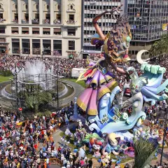 Gigantescas figuras de las mejores Fallas de Valencia, rodeadas de miles de personas, celebran la fiesta en una plaza con fuente.