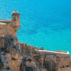 Torreón en el Castillo de Santa Bárbara, con el mar turquesa de fondo. Una vista icónica de la exposición alicantina.
