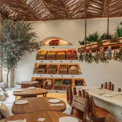 Interior de restaurantes en Valencia con encanto, con estanterías de frutas y verduras frescas, un olivo y mesas de madera.