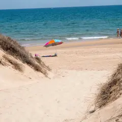 Dunas de arena y mar azul en el mareny de Sant Llorenç. Una sombrilla colorida y dos personas pasean por la orilla.