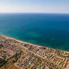 Vista aérea de la playa de arena de Dénia, con el mar azul turquesa y edificios residenciales.