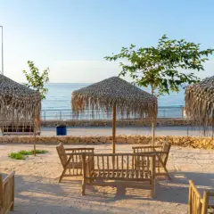 Mesas de madera y sombrillas de paja en la cala Lanuza, listas para disfrutar del mar y el sol.