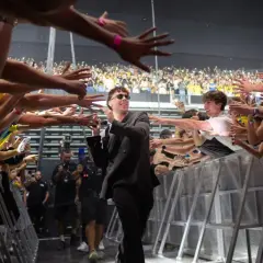 Quevedo saluda a sus fans en un concierto, con manos extendidas y móviles grabando el momento.