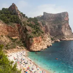Una cala rocosa con aguas turquesas, gente disfrutando del sol y el mar. Un paraíso entre las mejores playas de la Costa Blanca.