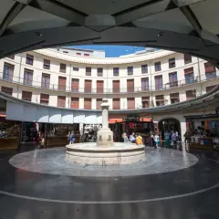 Fuente central en la plaza redonda valencia, rodeada de edificios curvos y puestos de venta.