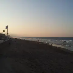 Gente pasea por la **playa de Piles** al atardecer, con el mar y el cielo en tonos pastel.