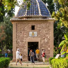 La ermita de Sant Jordi, con su cúpula azul y fachada de piedra, recibe a visitantes entre exuberante vegetación.