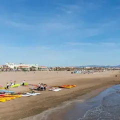 Gente prepara kayaks y tablas en la playa Malvarrosa, lista para un día de sol y mar.